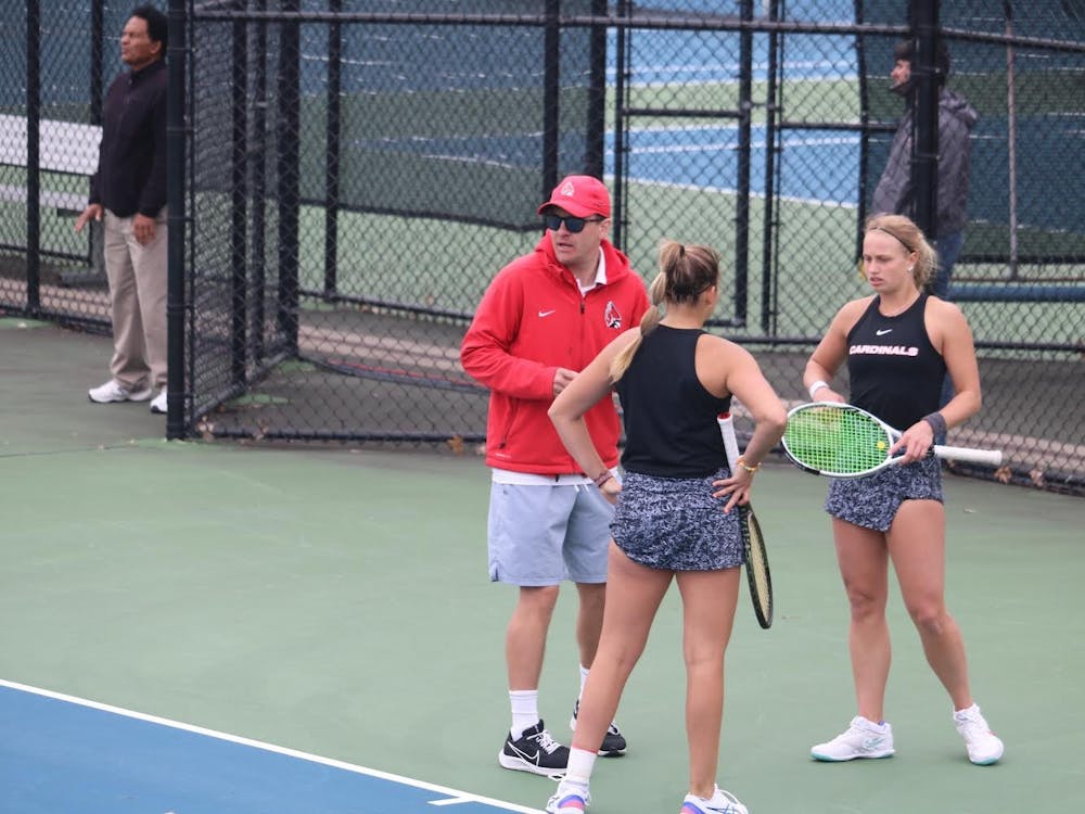 Head coach Max Norris meets with junior Amy Kaplan (left) and senior Hannah Davies (right) in the middle of their doubles match against Buffalo at Cardinal Creek Tennis Courts on April 30, 2022. Their match went unfinished as the Cardinals had already won 2/3 doubles matches en route to a berth in the MAC Championship. Corbin Hubert, DN
