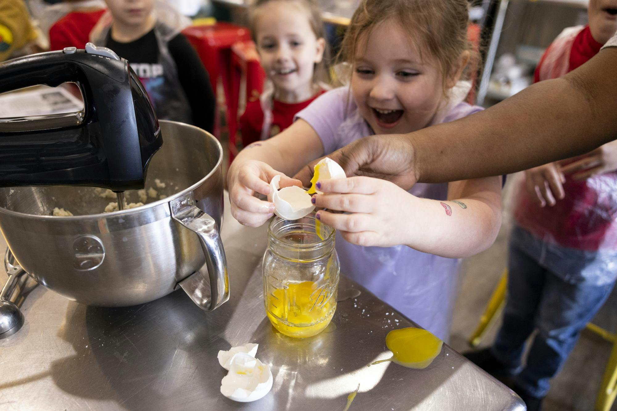 Carys Buzzard cracks an egg, with some spill, into a jar for her cookie dough batter for Santa at Now You're Cooking Culinary on Dec. 23, 2023 in Chesapeake, Virginia. (Billy Schuerman / The Virginian-Pilot)