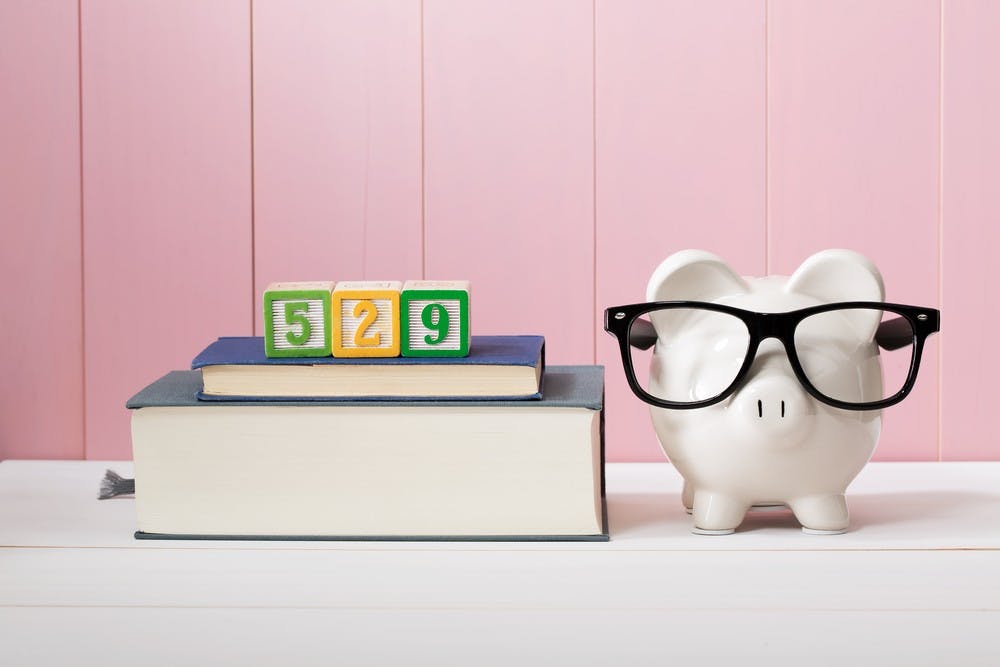 529 college savings and paying for education concept with piggy bank wearing eyeglasses alongside textbooks 