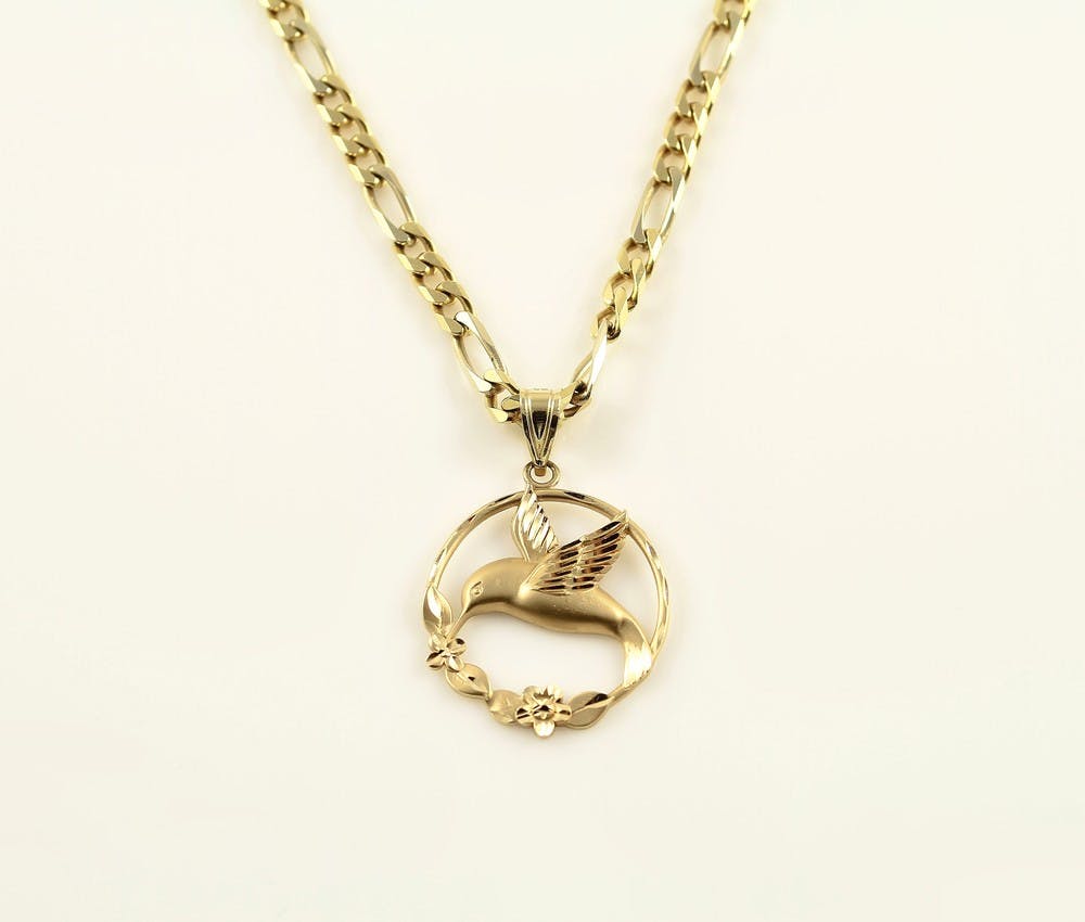 A shot of a gold necklace with design and round mockingbird pendant with flowers on white background