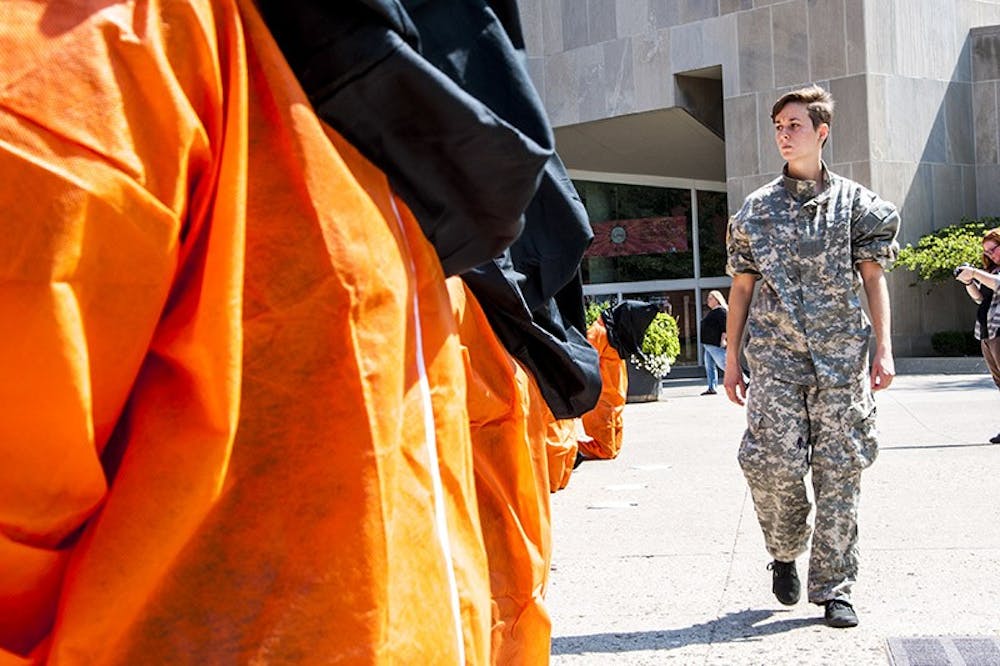 Senior telecommunications major Bianca Russelburg, dressed in military attire, paces infront of mock Guantanamo Bay detainees in front of Bracken Library on Aug. 28. Amnesty International organized the protest to bring attention to practices at the American detention center. DN PHOTO JONATHAN MIKSANEK