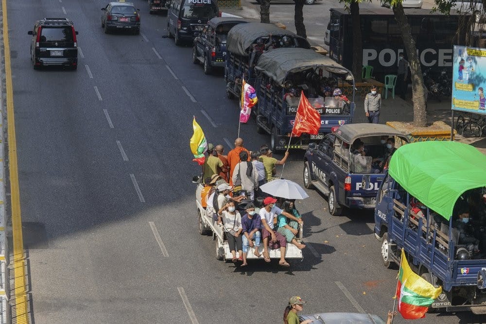 A vehicle with Myanmar and military flags and supporters of the Myanmar military and the military-backed Union Solidarity and Development Party passes by a row of police trucks with police security onboard parked near the Kyauktada police station in Yangon, Myanmar Monday, Feb. 1, 2021. Myanmar military television said Monday that the military was taking control of the country for one year. (AP Photo)