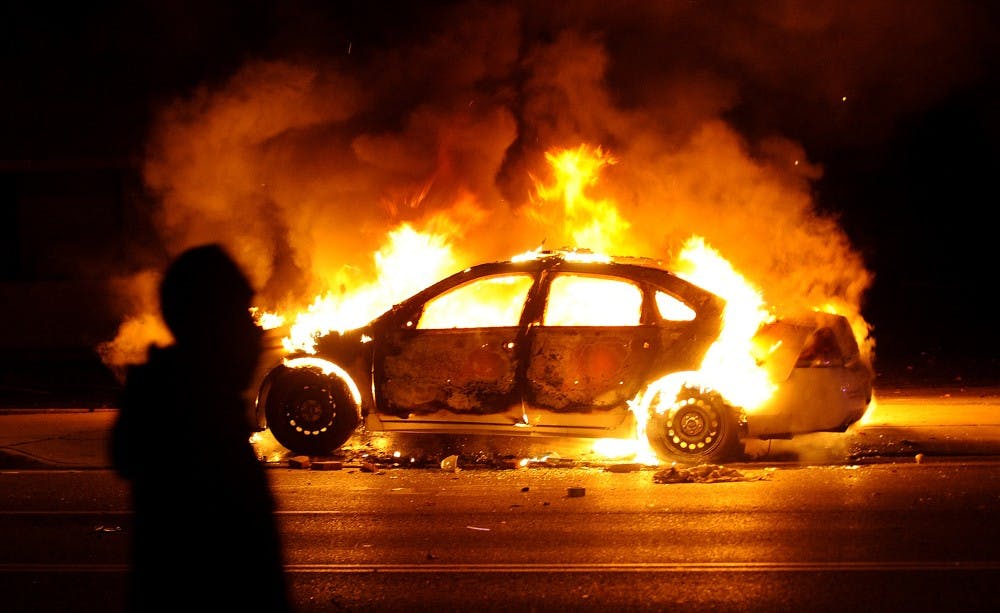 A protester walks by a St. Louis County police car that was set on fire along South Florissant Road in Ferguson following the announcement of the grand jury decision on Monday, Nov. 24, 2014. (Wally Skalij/Los Angeles Times/TNS)