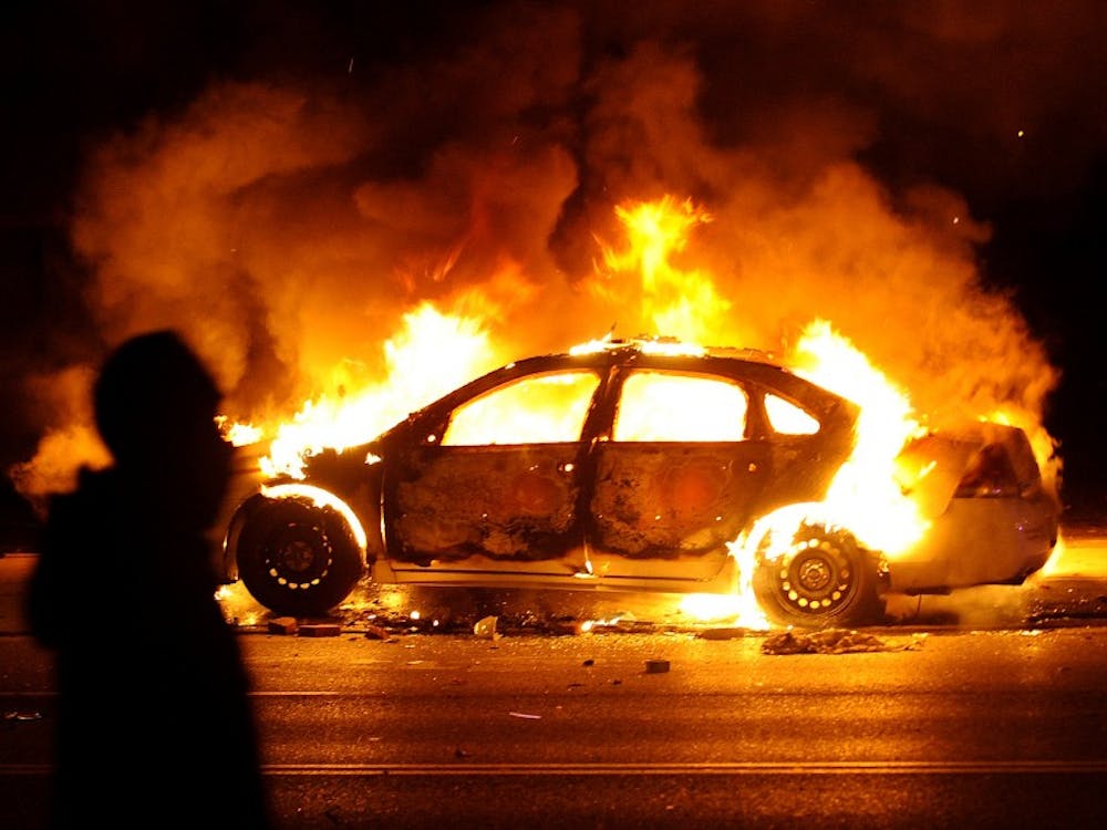 A protester walks by a St. Louis County police car that was set on fire along South Florissant Road in Ferguson following the announcement of the grand jury decision on Monday, Nov. 24, 2014. (Wally Skalij/Los Angeles Times/TNS)