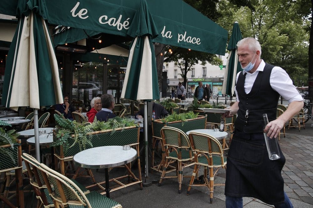 A waiter walks to serve customers at a restaurant, June 15, 2020, in Paris. Paris is rediscovering itself, as its cafes and restaurants reopen for the first time since the fast-spreading virus forced them to close their doors March 14. (AP Photo/Francois Mori)