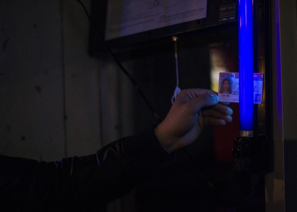<p>Como Negrete, a senior accounting major, holds up a fake ID to a black light on the wall at The Chug in the Village. The Chug kept losing the UV pens, and the UV light on the wall discourages more people from attempting to pass through with a fake ID. <em>DN PHOTO BREANNA DAUGHERTY</em></p>