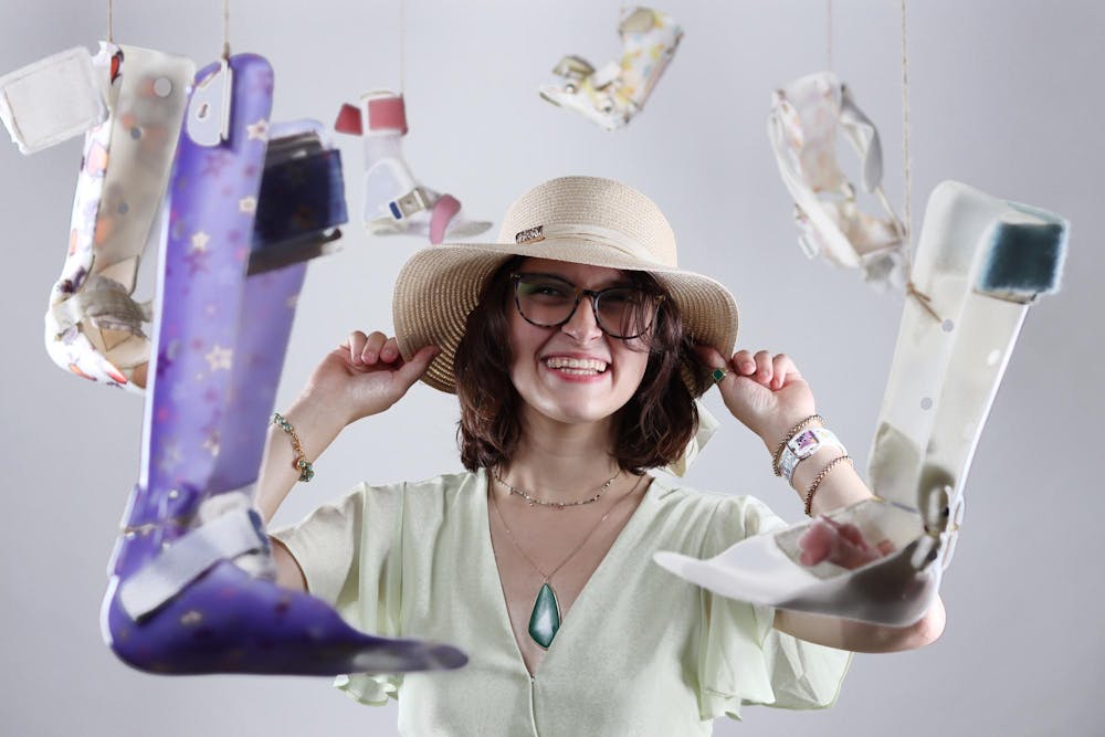 Katherine Hill poses for a photo in her garage July 6. Hill was surrounded by leg braces suspended in the air, wearing her favorite sunhat. Isaiah Wallace, DN