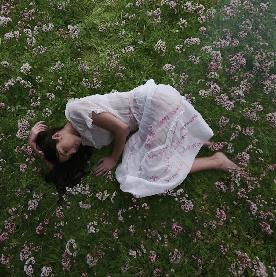 Olivia Rodrigo is wearing a white dress and laying in a field of flowers.