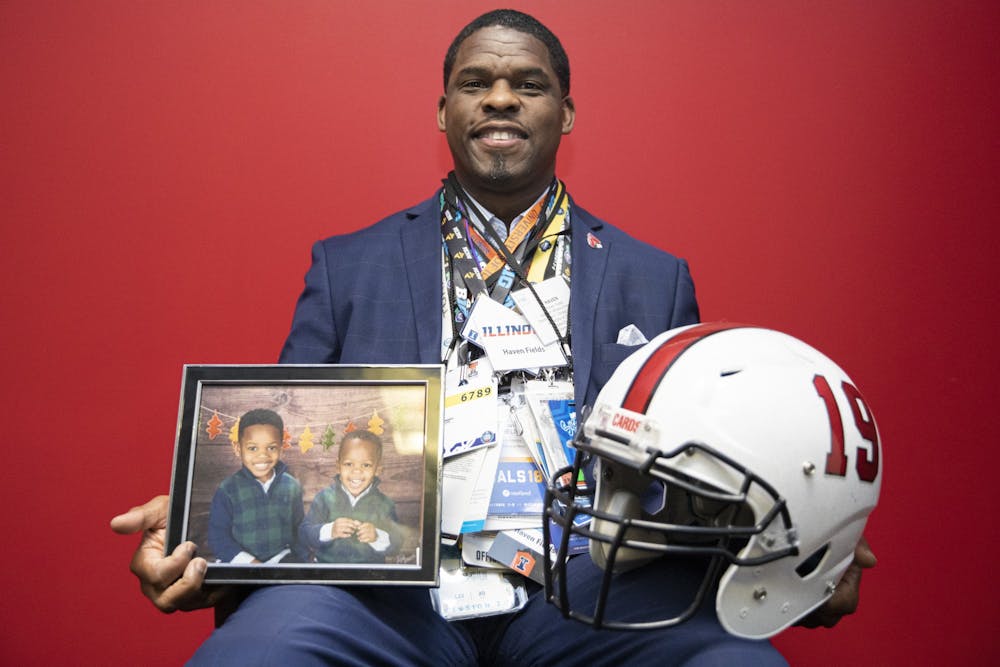 Haven Fields, deputy athletic director poses for a portrait wearing all of his press passes and holding a Ball State football helmet and a portrait of his two sons, April 19, 2021, in his office in the Health and Physical Activity building. Jacob Musselman, DN
