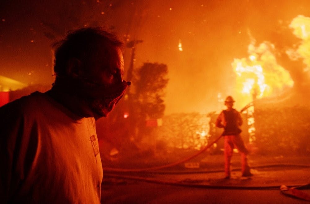 A man walks past a burning home during the Getty fire, Oct. 28, 2019, in Los Angeles, Calif. (AP Photo/ Christian Monterrosa)
