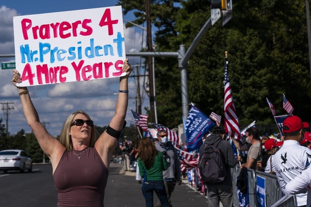Karen Simon from the District of Columbia, left, waves a banner together with other supporters of President Donald Trump, gathered outside the Walter Reed National Military Medical Center in Bethesda, Md., Monday, Oct. 5, 2020. Trump said Monday he's leaving the military hospital where he has been treated for COVID-19 and will continue his recovery at the White House. (AP Photo/Manuel Balce Ceneta)