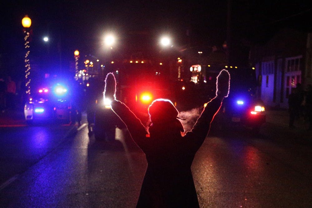 A protester raises her hands in the street as police use tear gas to try to take control of the scene near a Ferguson Police Department squad car after protesters lit it on fire on Nov. 25 in the wake of the grand jury decision not to indict officer Darren Wilson in the shooting death of Ferguson, Mo., teen Michael Brown. MCT PHOTO