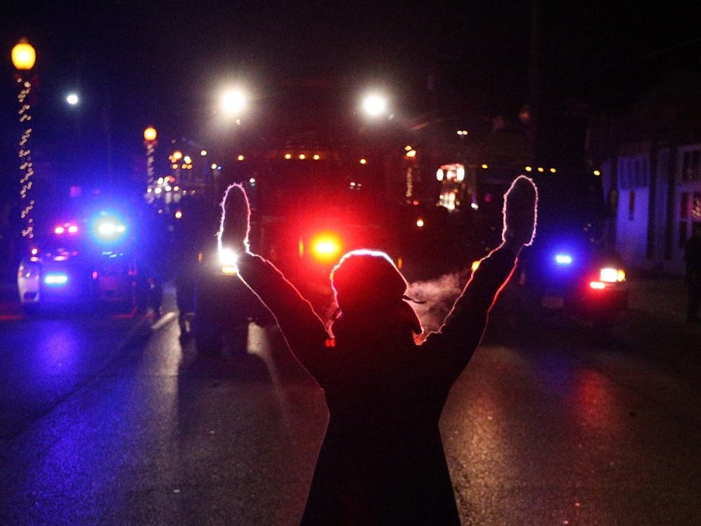 A protester raises her hands in the street as police use tear gas to try to take control of the scene near a Ferguson Police Department squad car after protesters lit it on fire on Nov. 25 in the wake of the grand jury decision not to indict officer Darren Wilson in the shooting death of Ferguson, Mo., teen Michael Brown. MCT PHOTO