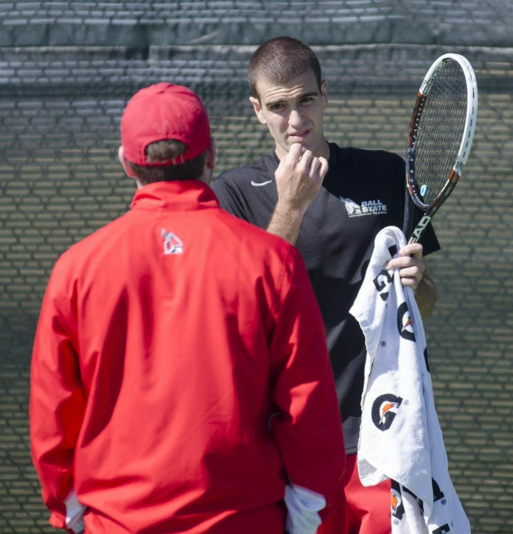Junior Patrick Elliott talks to volunteer assistant coach Ryan Baxter during his match against Toledo on March 30 at the Cardinal Creek Tennis Courts. DN PHOTO BREANNA DAUGHERTY