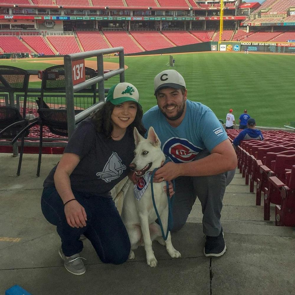 Sean White, student assistant coordinator, poses with his wife, Heidi, and his husky, Nanuk, May 14, 2019, at the "Bark in the Park" event for the Cincinnati Reds vs. Chicago Cubs game. White said he calls Nanuk "Nana," and she is enjoying the extra attention she is getting because he is home due to COVID-19 concerns. Sean White, Photo Provided
