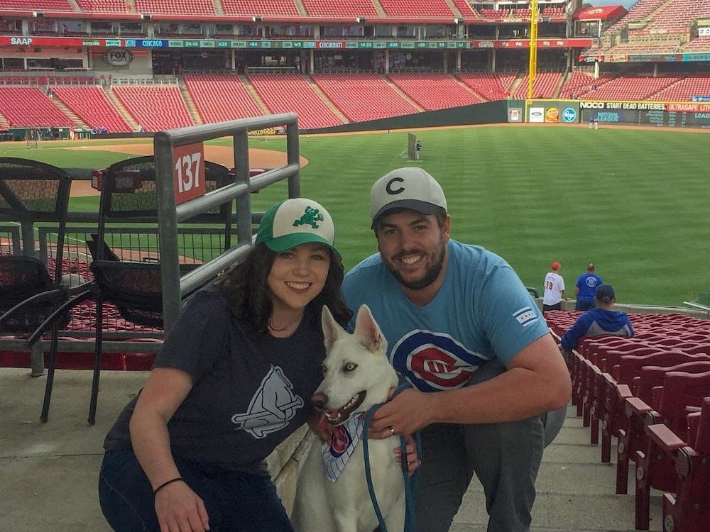 Sean White, student assistant coordinator, poses with his wife, Heidi, and his husky, Nanuk, May 14, 2019, at the "Bark in the Park" event for the Cincinnati Reds vs. Chicago Cubs game. White said he calls Nanuk "Nana," and she is enjoying the extra attention she is getting because he is home due to COVID-19 concerns. Sean White, Photo Provided