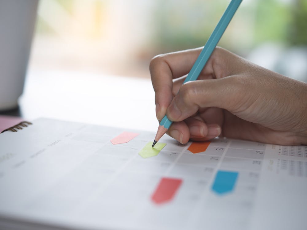 Close-up of business woman taking note on 2022 calendar desk, making agenda on office table. Event planner timetable. Calendar event plan, work schedule planning