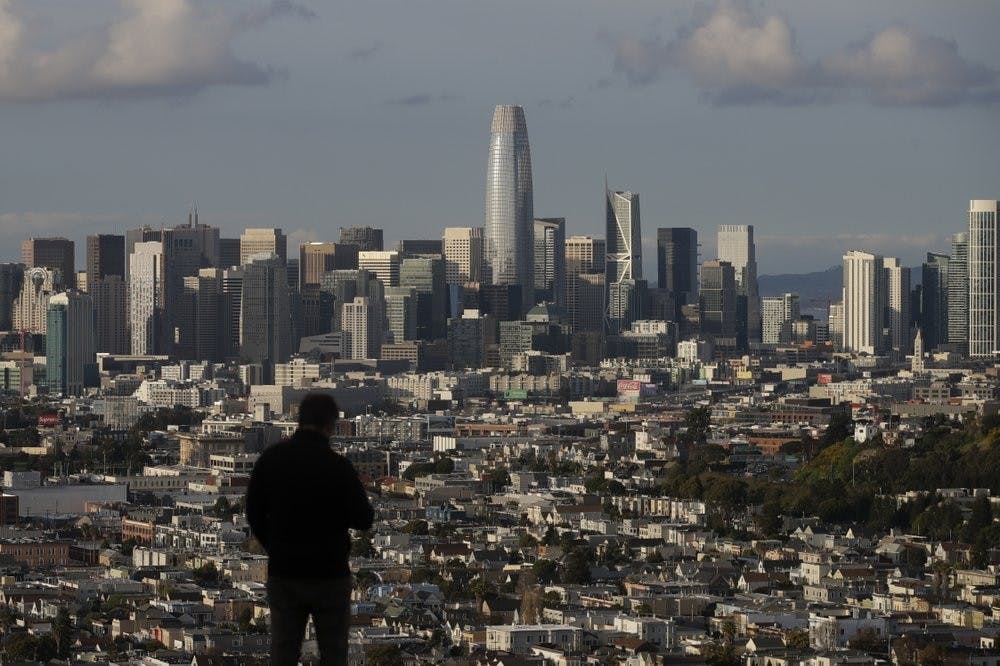 A man looks toward the skyline from Bernal Heights Hill in San Francisco, March 16, 2020. Officials in six San Francisco Bay Area counties issued a shelter-in-place mandate Monday affecting nearly 7 million people, including the city of San Francisco itself. (AP Photo/Jeff Chiu)