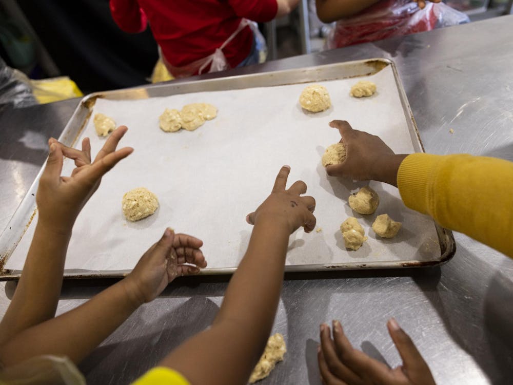 Children reach their freshly rolled balls of cookie dough onto a baking sheet for Santa during a class at Now You're Cooking Culinary on Dec. 23, 2023 in Chesapeake, Virginia. (Billy Schuerman / The Virginian-Pilot)