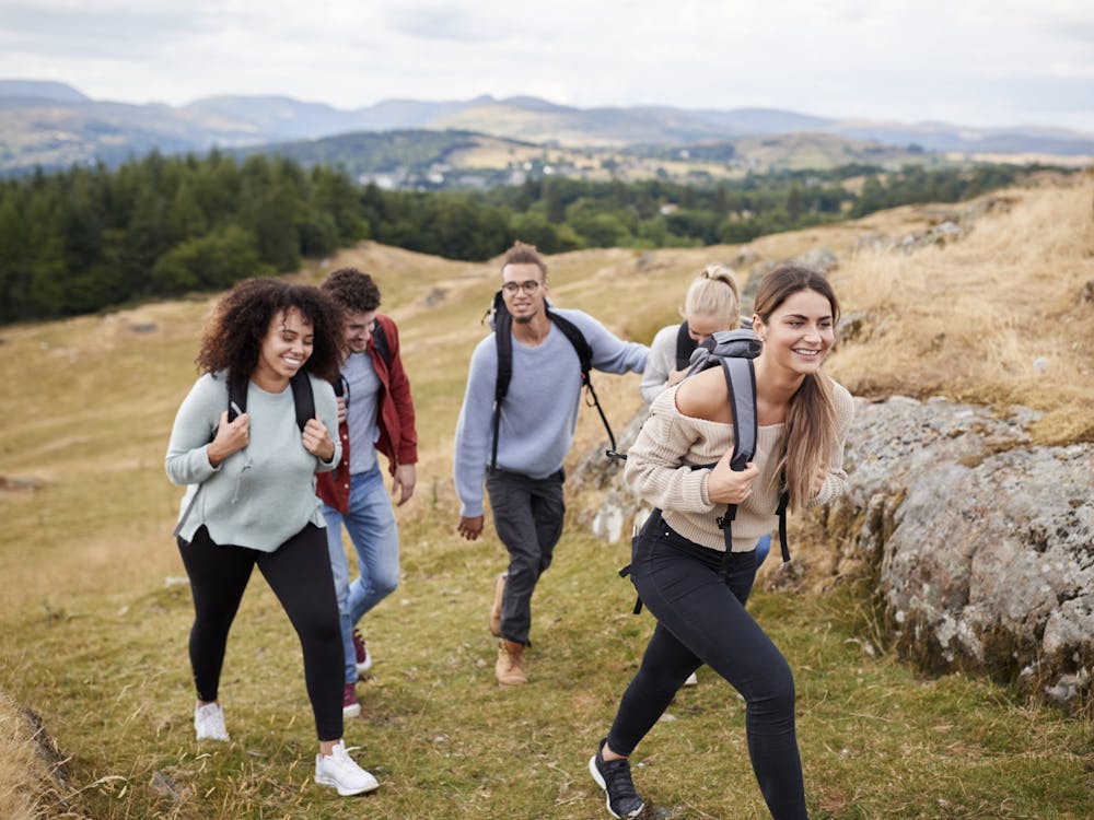 Multi ethnic group of five young adult friends hiking across a field uphill towards the summit, close up