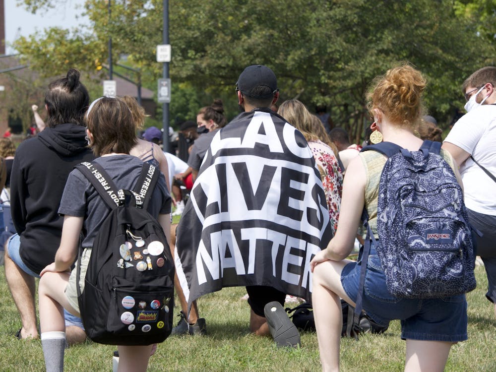 A protestor wears a "Black Lives Matter" flag while kneeling in memory of George Floyd on the University Green Aug. 25. This demonstration was organized two days after police officers in Kenosha, Wisconsin shot Jacob Blake in the back seven times. John Lynch, DN