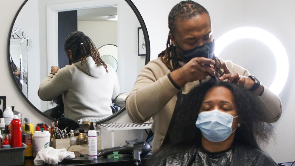 Che Hopkins, owner of Meraki Style Studio, parts Rachelle Joyner’s hair to blow dry for a silk press March 12, 2021. Joyner said she drove from Indianapolis, Indiana, to get her hair down by Hopkins as he has been her stylist for 13 years. Sumayyah Muhammad, DN.