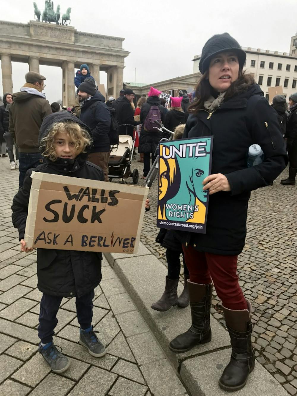 <p>A ten-year-old in front of the Brandenburg Gate holds a protest sign reading "Walls suck / Ask a Berliner" at the Women's March. Berliners view Trump with concern since the United States is important to Germany.</p>