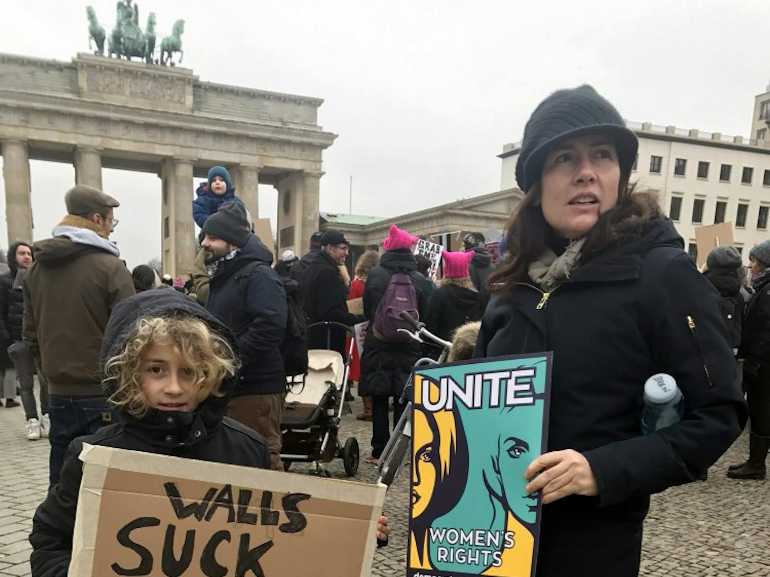 A ten-year-old in front of the Brandenburg Gate holds a protest sign reading "Walls suck / Ask a Berliner" at the Women's March. Berliners view Trump with concern since the United States is important to Germany.