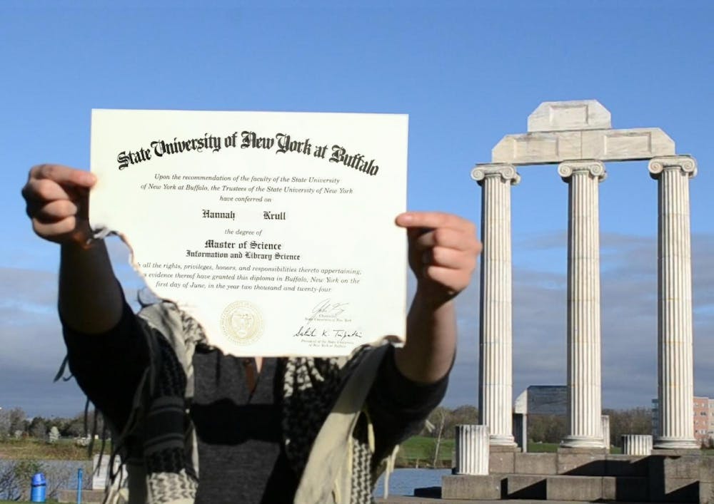 A student holds up a damaged UB diploma in front of the pillars at Baird Point.