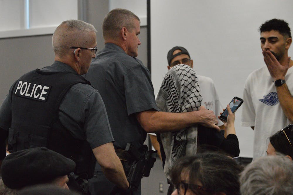 UPD officers escort a pro-Palestine protester out of UB SSI's event as a IDF soldier blows her an air-kiss. 