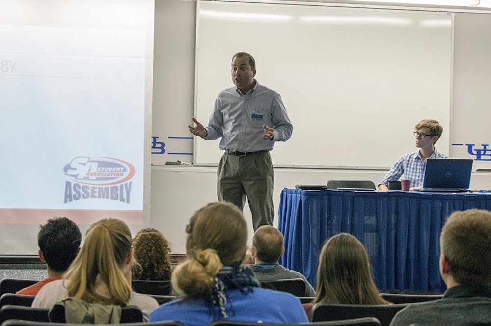<p>Chris Clune (middle), director of UBIT customer service, speaks during Wednesday's Student Association Assembly meeting as Speaker James Corra (far right) listens. It was SA Assembly's first meeting of the semester. </p>