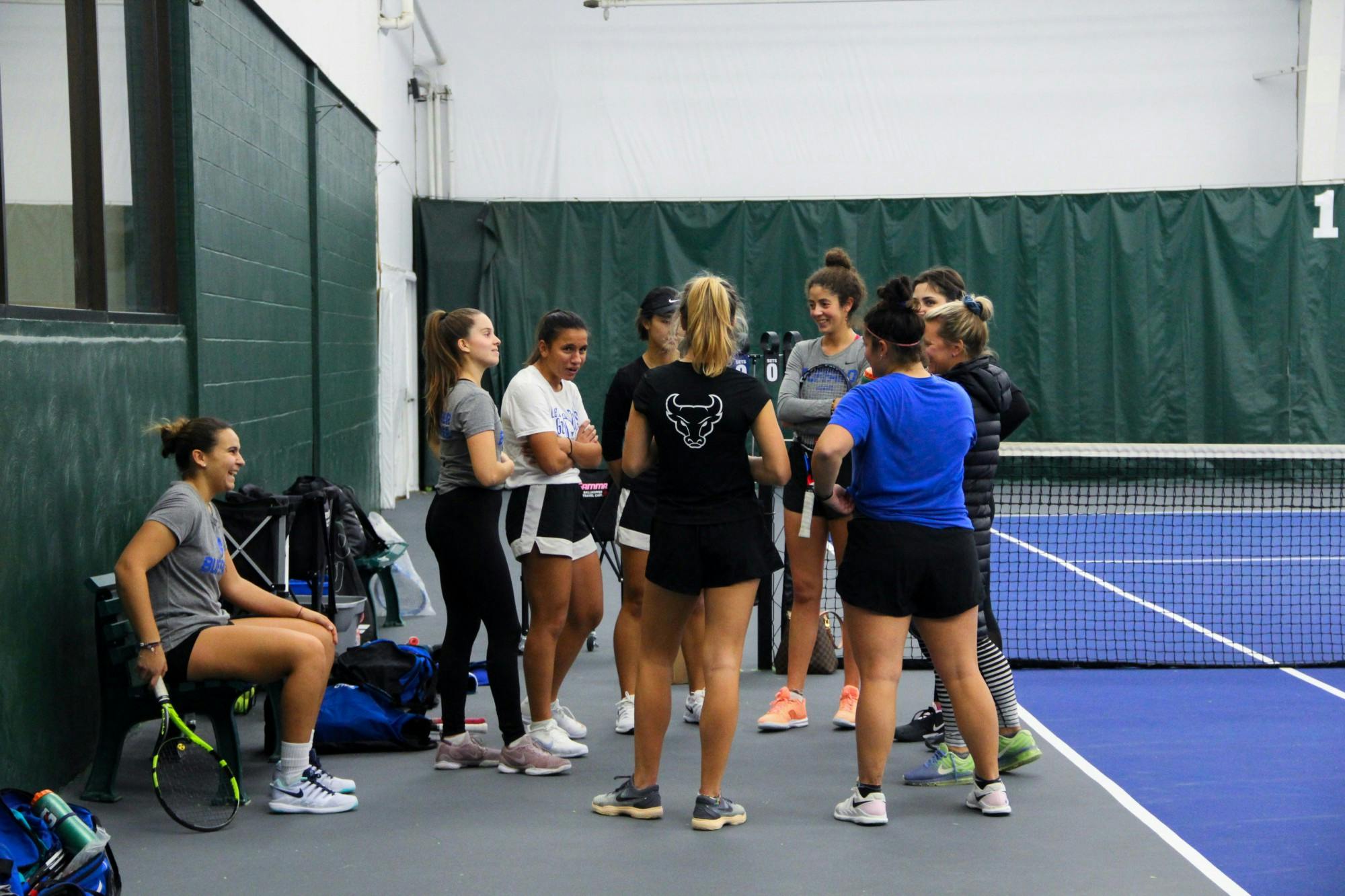 Eight of the nine members of UB’s fully-international women’s tennis team gather around head coach Kristen Maines during practice.