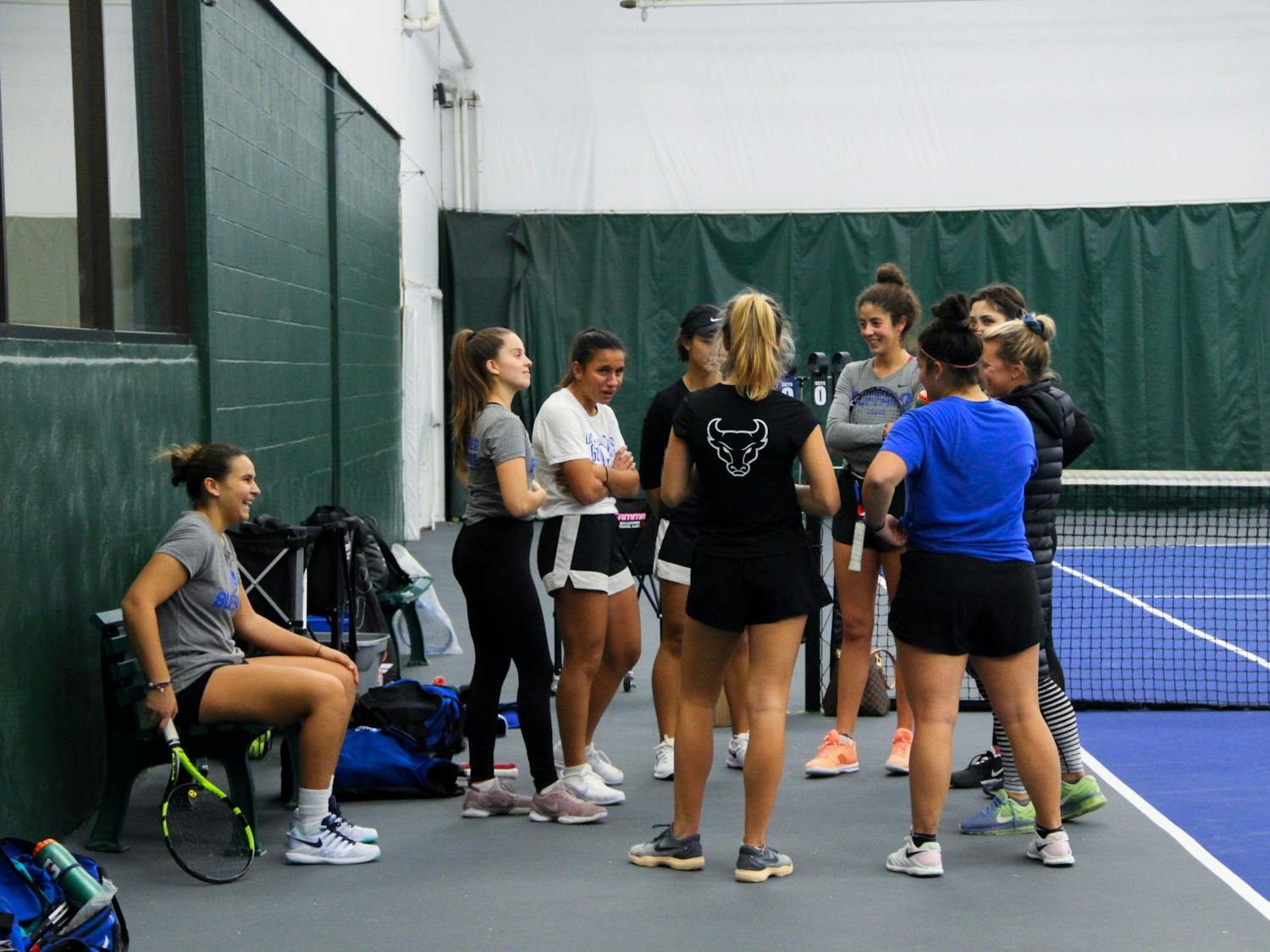 Eight of the nine members of UB’s fully-international women’s tennis team gather around head coach Kristen Maines during practice.