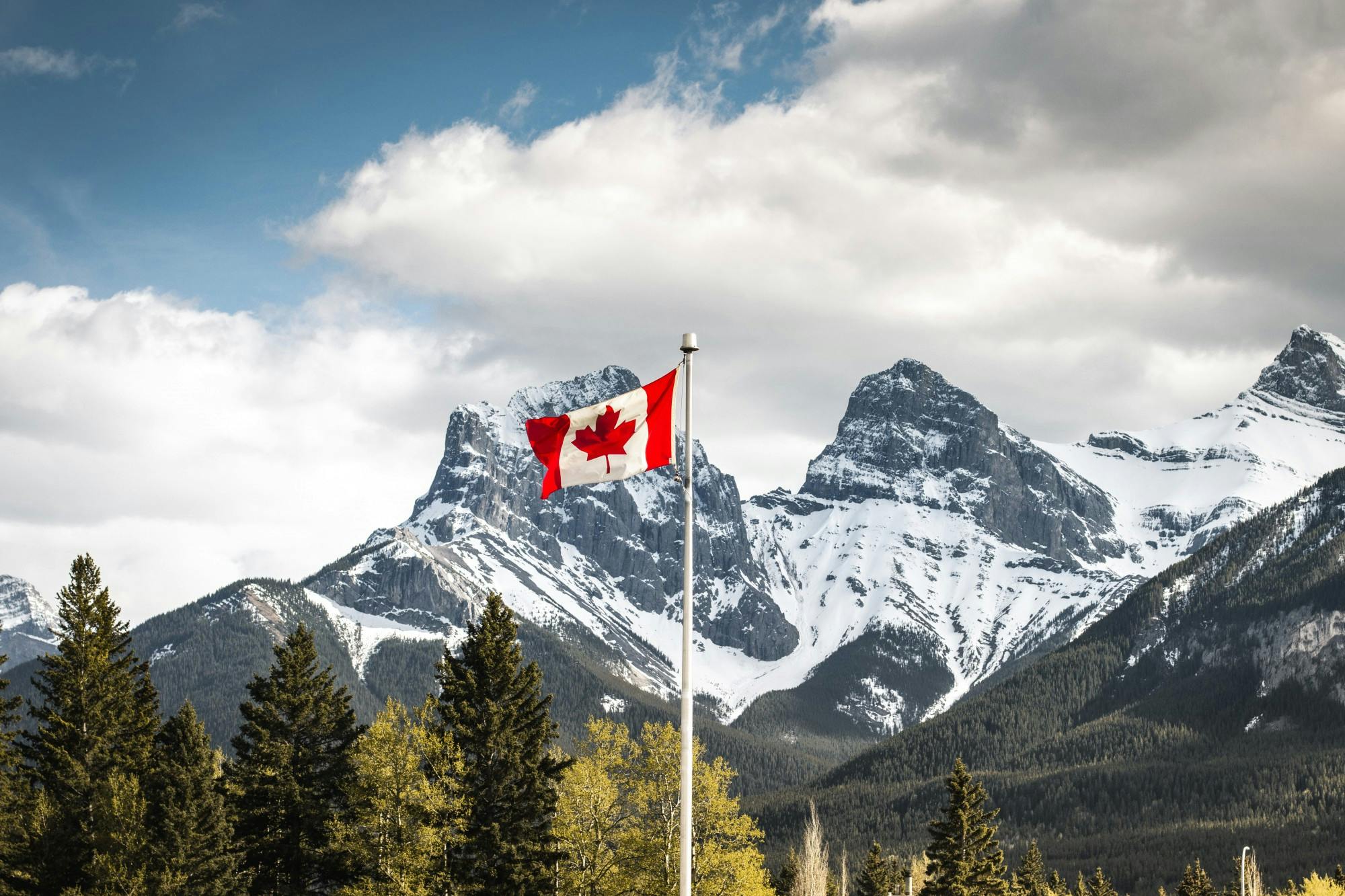 A Canadian flag with Three Sisters in Alberta, Canada in the background.
