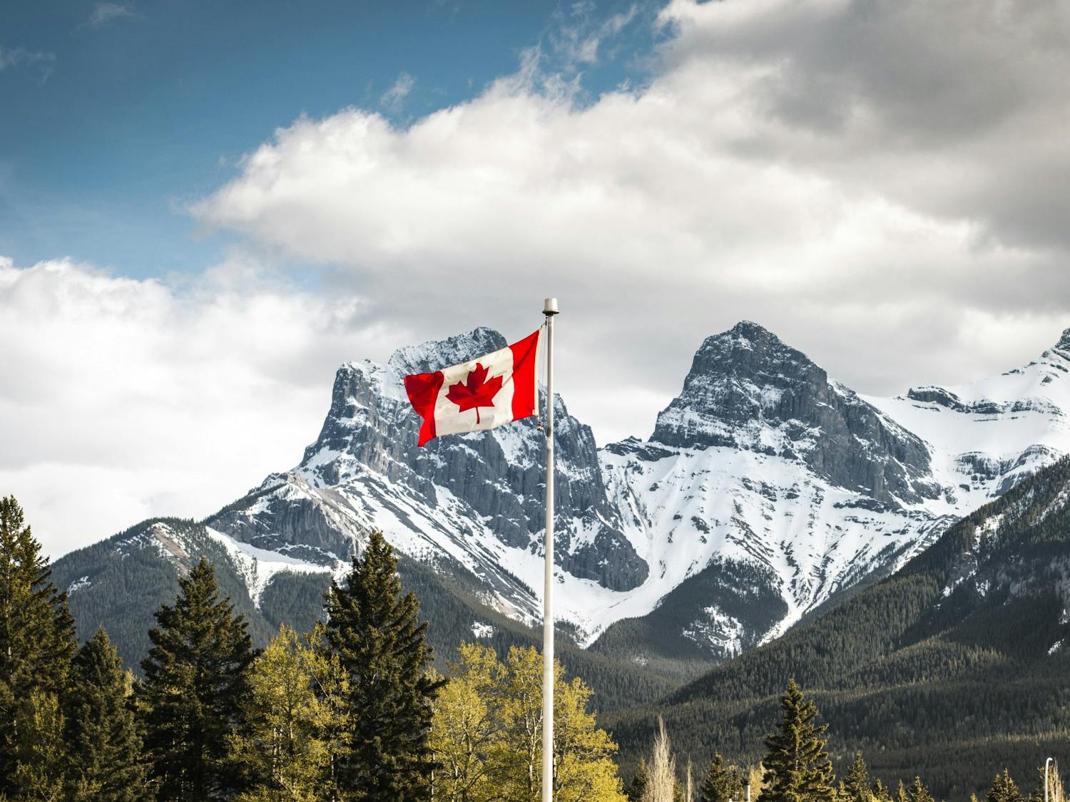 A Canadian flag with Three Sisters in Alberta, Canada in the background.