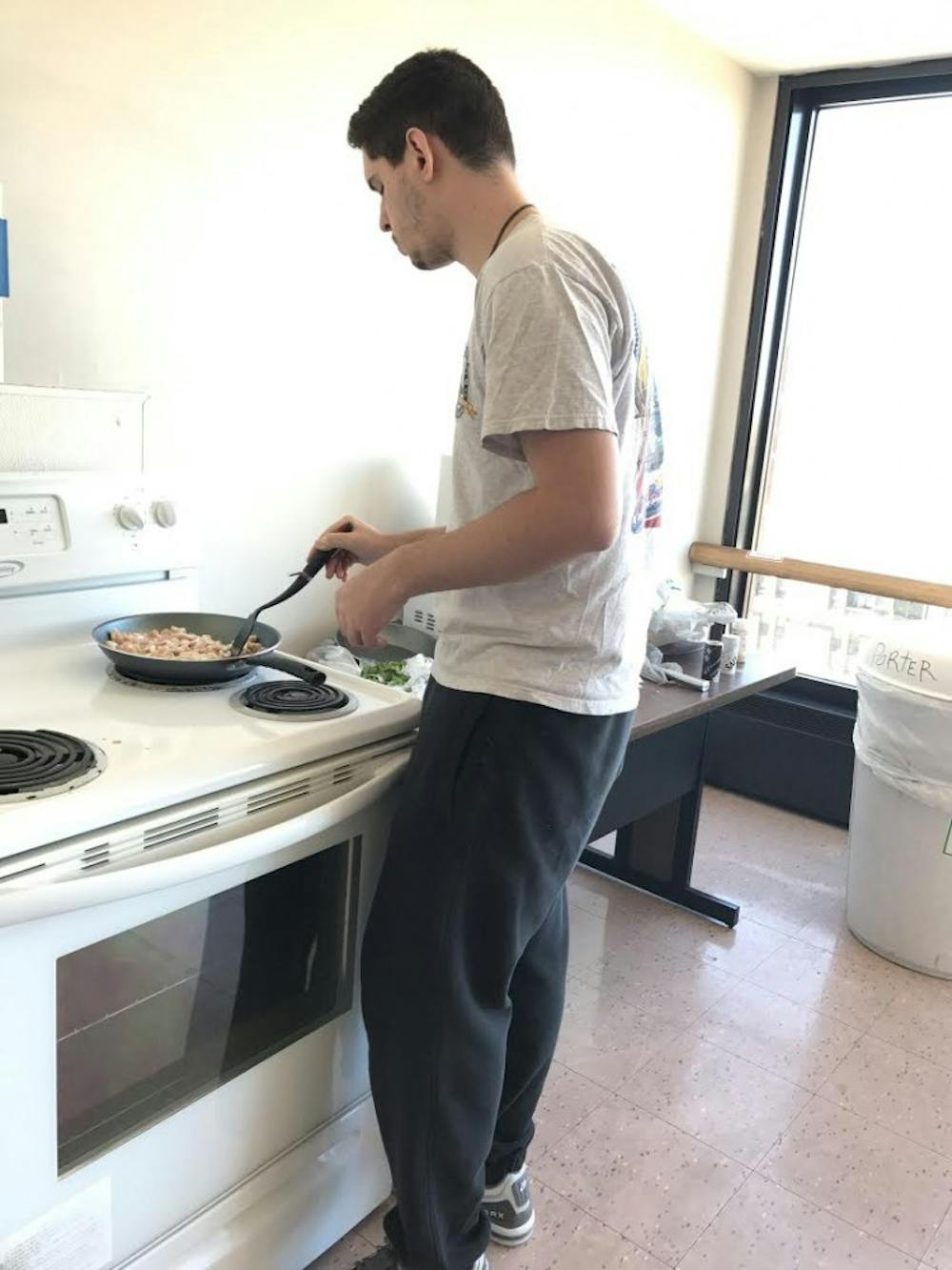<p>Gabriel Periera cooks at the stove in Porter Hall’s kitchen. Periera was born in Uruguay, and enjoys cooking traditional Uruguayan food.</p>