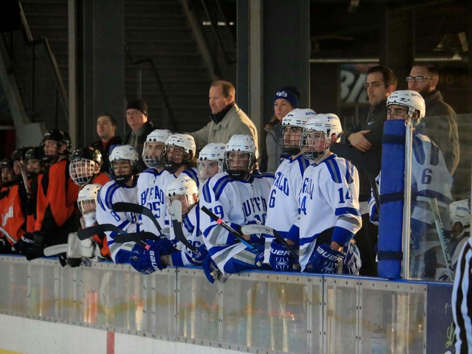 The club hockey team rest on the bench during a game. the team deals with multiple challenges being a club sport.