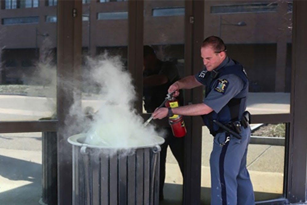 <p>UPD Officer David Stall uses a fire extinguisher to put out a garbage can fire outside the Student Union on April 17. Assistant Chief of Police Chris Bartolomei recently attended a three-day training targeted to fight against implicit bias in policing.</p>