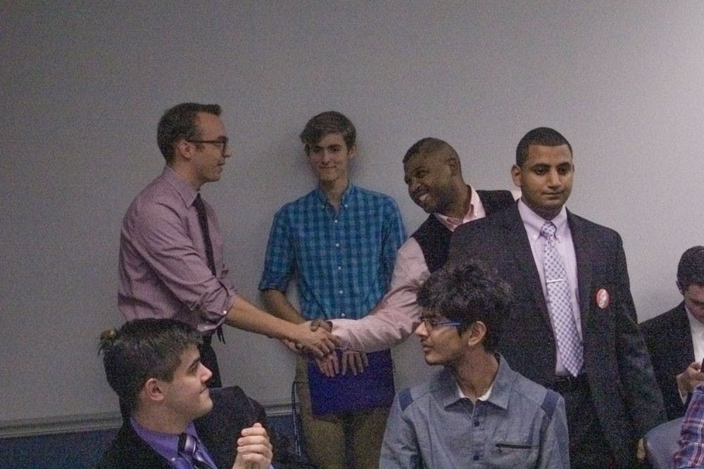 <p>Newly elected Senate Chair Dillon Smith (standing far left) shakes hands with fellow candidate Carl Ross (middle) after winning the senate chair election, as losing candidate Yaser Soliman (far right) looks on in dismay. Soliman is challenging the results of the election.</p>