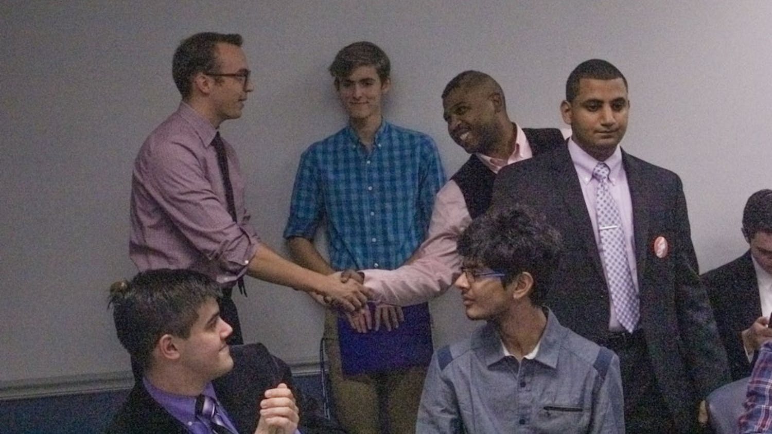 Newly elected Senate Chair Dillon Smith (standing far left) shakes hands with fellow candidate Carl Ross (middle) after winning the senate chair election, as losing candidate Yaser Soliman (far right) looks on in dismay. Soliman is challenging the results of the election.
