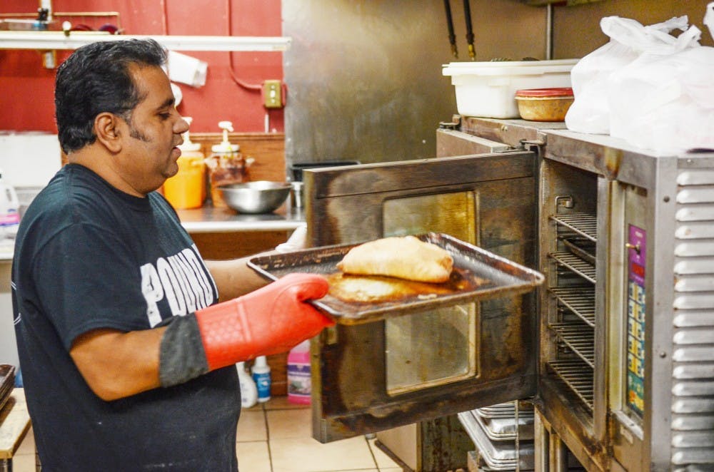 <p>MD B Ali, owner of Calios, takes a calzone out of the oven at the Main Street location. Calios provides those looking for food around South Campus with a variety of calzones, including dessert-style.</p>