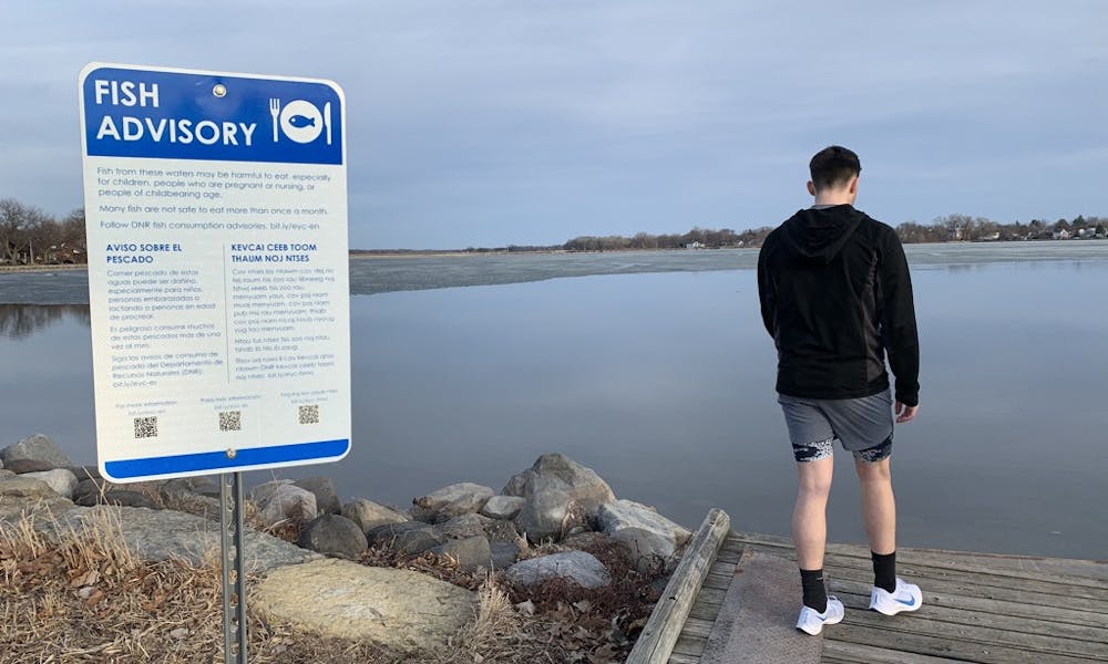 Photo of a fish advisory sign and a man on a pier looking out towards Lake Monona.