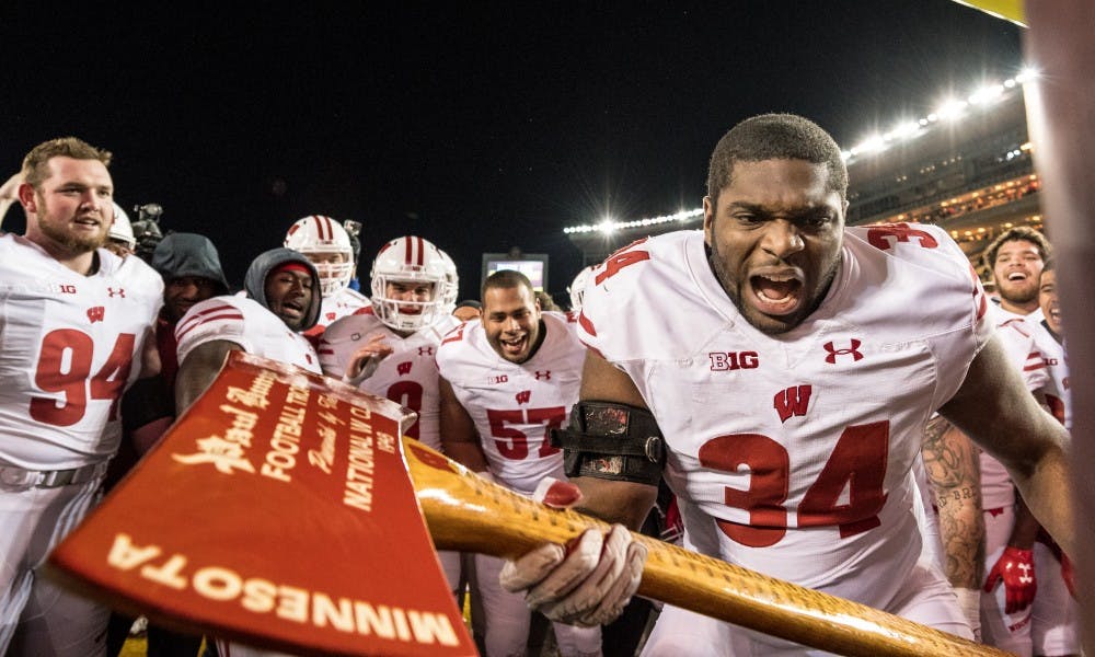Chikwe Obasih (34)&nbsp;chops down the goal post with Paul Bunyan's Axe following Wisconsin's 31-0 victory over Minnesota, completing their perfect 12-0 regular season.