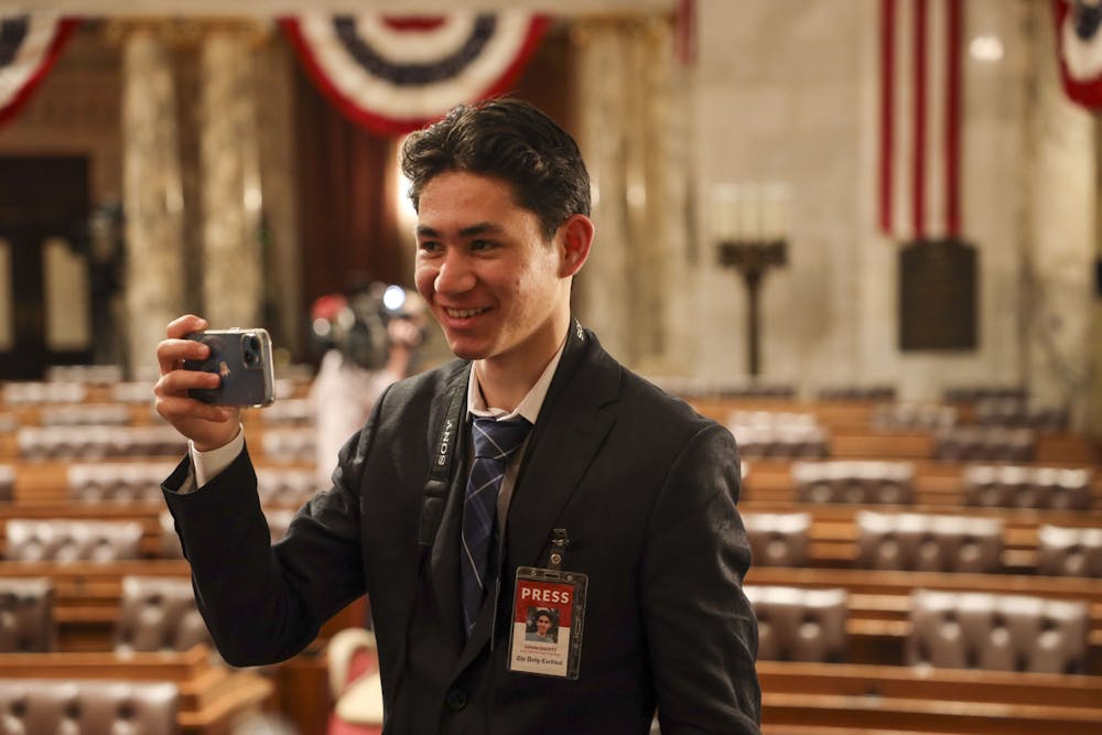 Cardinal senior staff writer and "Cardinal Call" host Gavin Escott takes a photo on his phone at Gov. Tony Evers' annual State of the State address in January 2023.