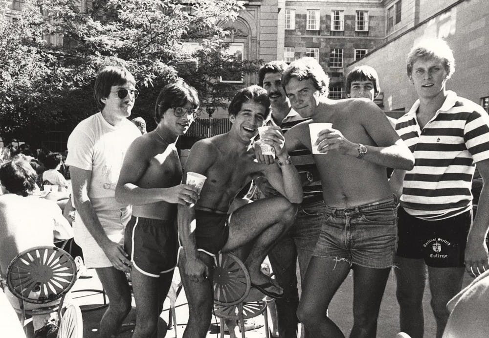 A group of guys in shorts, largely missing shirts, drink outside the Memorial Union.