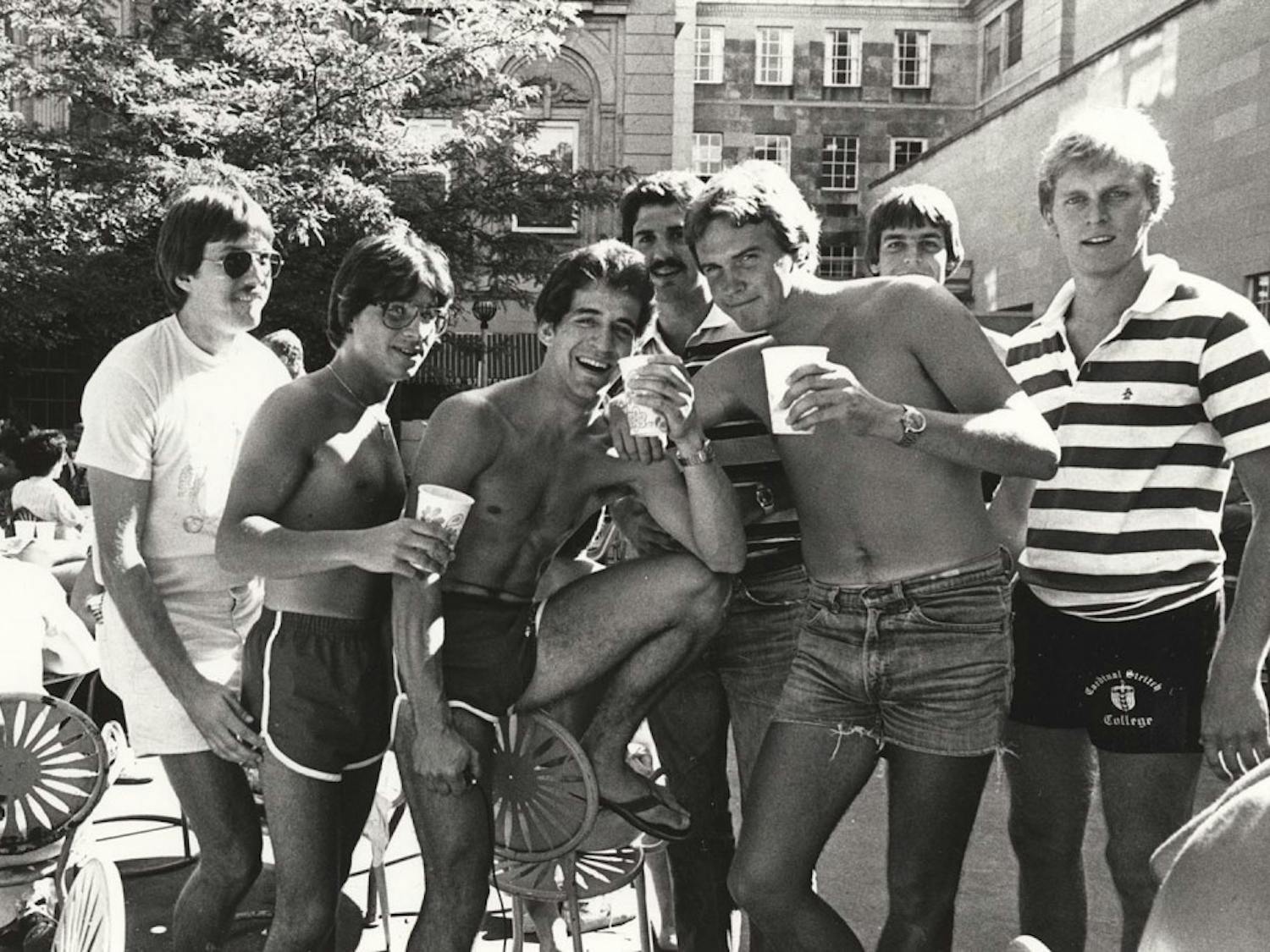 A group of guys in shorts, largely missing shirts, drink outside the Memorial Union.