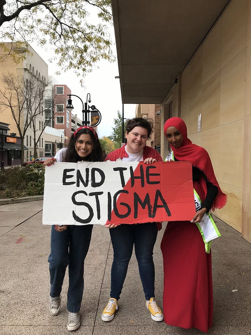Photo of three people holding up a sign that says "END THE STIGMA"