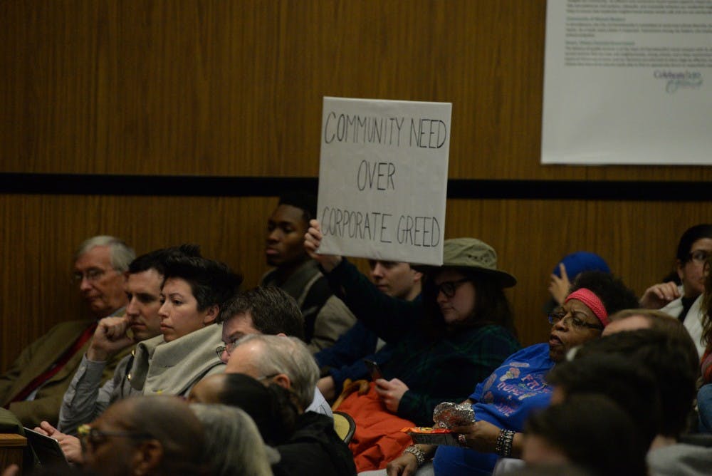 Attendees at the Council meeting hold a sign reading "Community need over corporate greed" in protest of the rejected West2nd special use permit.&nbsp;