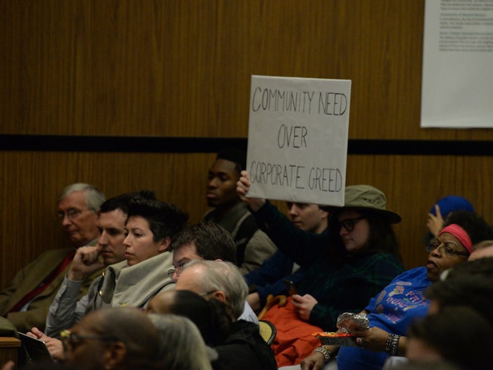 Attendees at the Council meeting hold a sign reading "Community need over corporate greed" in protest of the rejected West2nd special use permit.&nbsp;