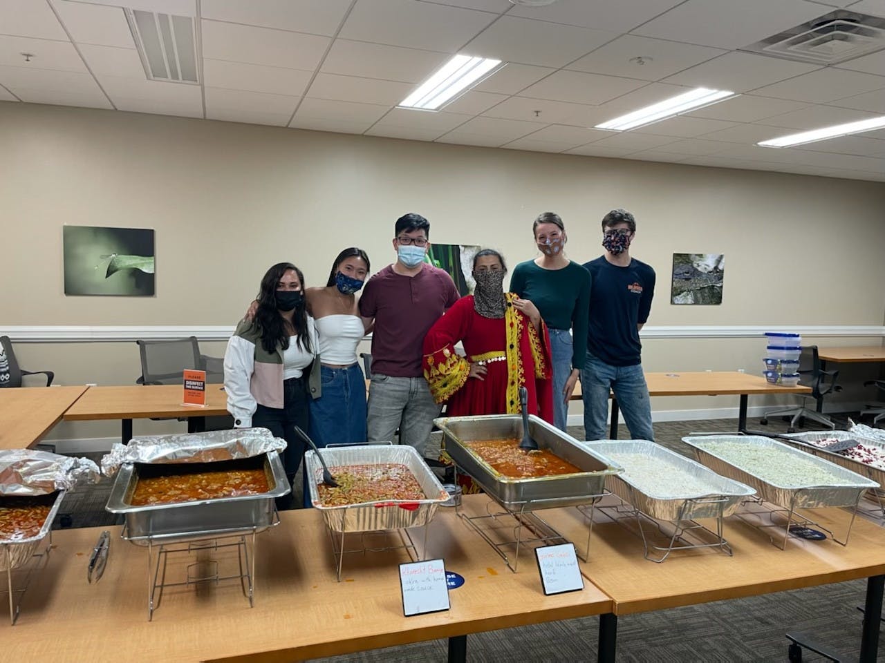 Taste of Home members stand with Chef Khadija behind an array of delicious Afghan cuisine.